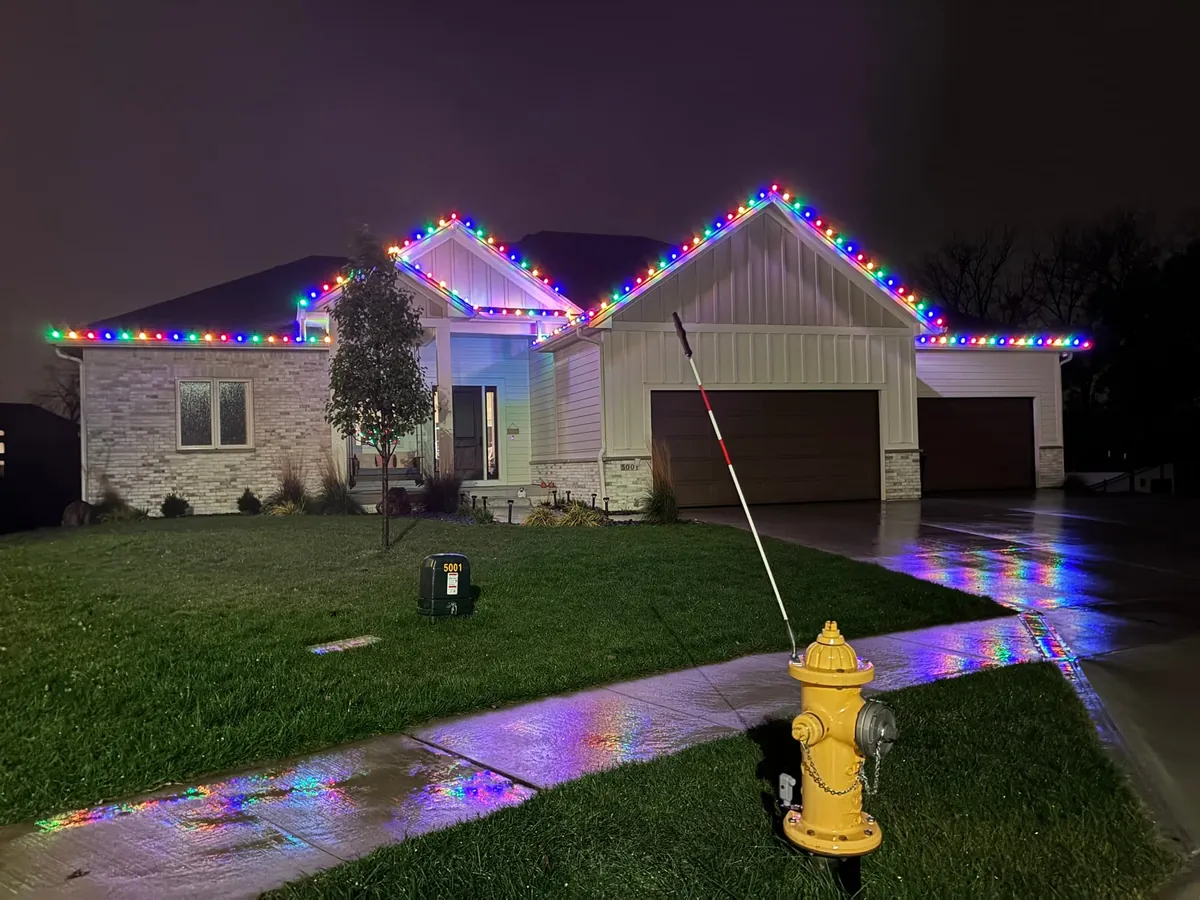 Multicolor C9 bulbs outlining the rooflines of a ranch home in West Des Moines, reflecting on a wet driveway